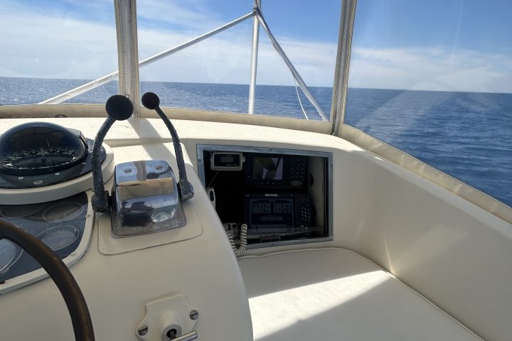 Inside a boat's cockpit with view of ocean and clear blue sky.