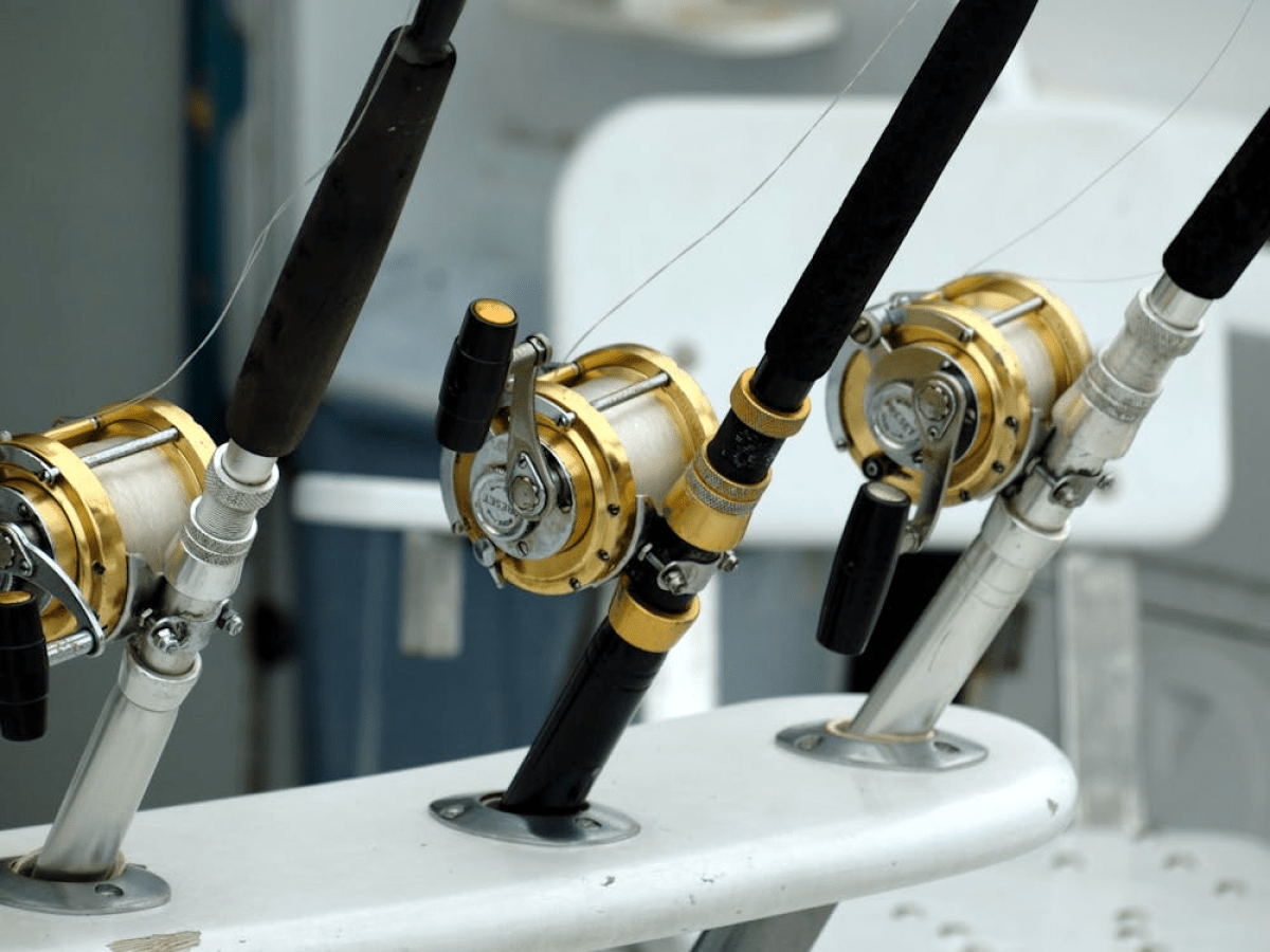 Three fishing rods with gold reels mounted on a boat.