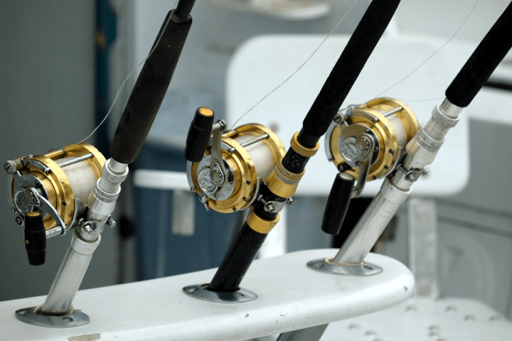 Three fishing rods with gold reels mounted on a boat.