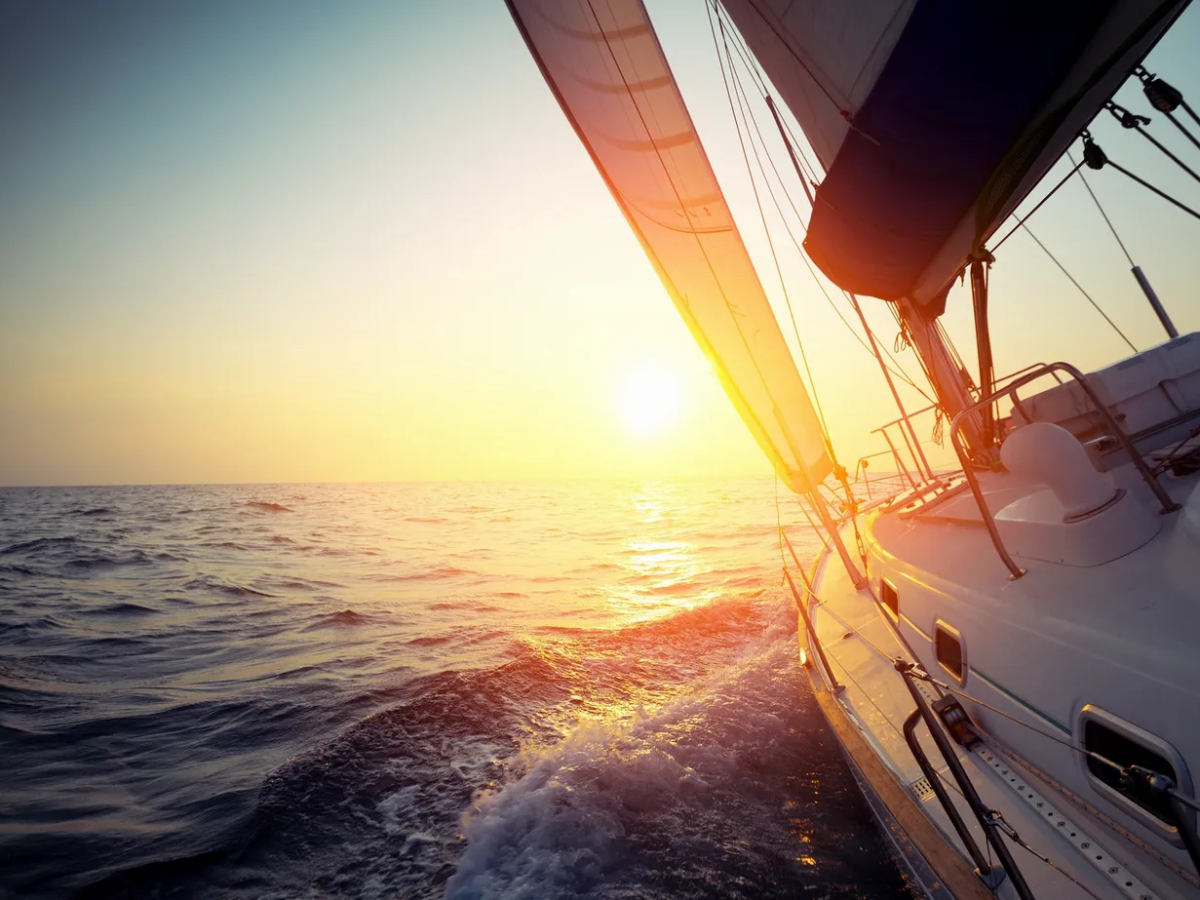 Sailboat on the ocean at sunset with the sun glowing over the water.